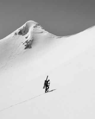 Photo en noir et blanc : Paysage de neige, un skieur remonte une pente de neige, skis sur le sac