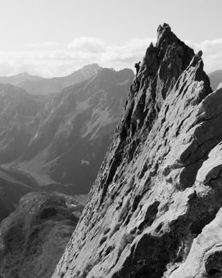 Photo en noir et blanc : Sur une arête rocheuse, abrupte, un grimpeur au loin