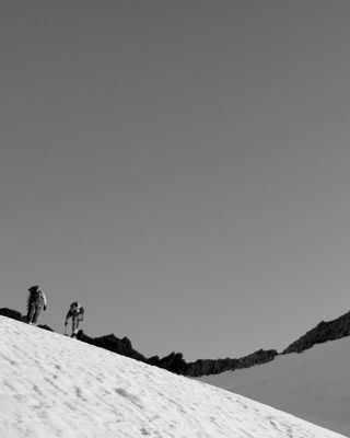 Photo en noir et blanc : Paysage de neige, rochers, deux alpinistes sur une pente de neige