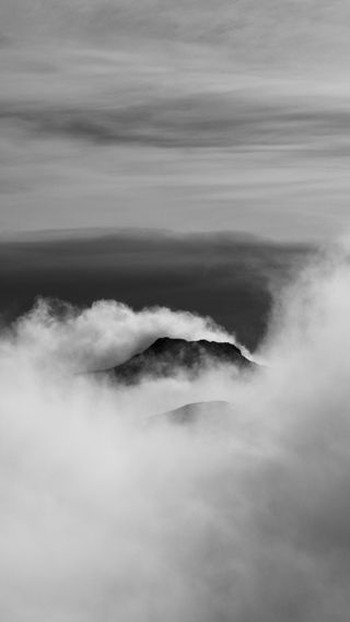 Photo en noir et blanc : deux montagnes dépassent de nuages bas